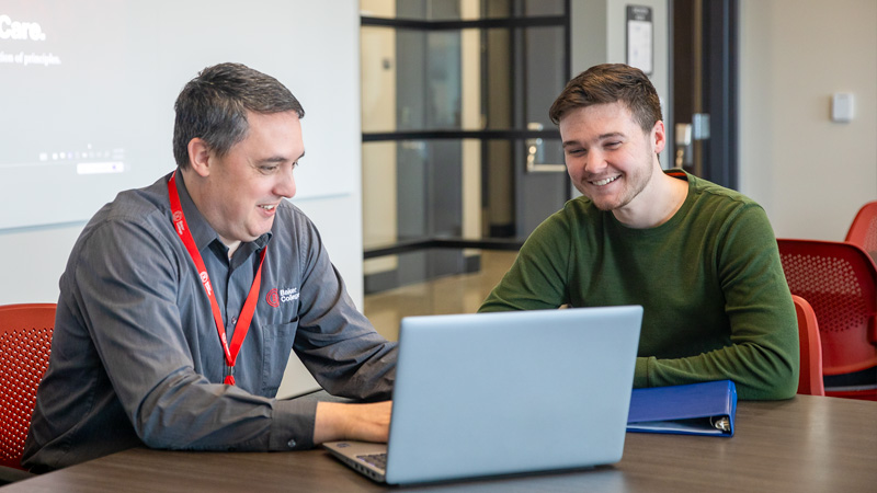 Financial Aid advisor and student smile as they look at a laptop.