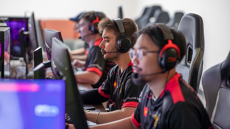 Three Esports players as seen from a side profile, all wearing headsets and looking at monitors